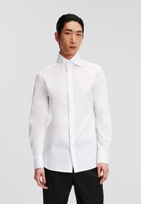 Witte lange mouwen shirt gemaakt van gladde stof met een klassieke kraag, knopen aan de voorkant en een getailleerde pasvorm, gecombineerd met zwarte broek.