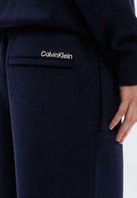 Σκούρο μπλε φούτερ παντελόνι με πλαϊνή τσέπη και κεντημένο λογότυπο Calvin Klein σε λευκό. Μαλακή υφή με σχεδίαση ίσιου ποδιού.