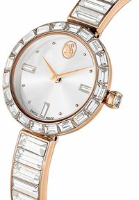 Montre en or rose avec un cadran rond, un cadran argenté et des accents en cristal. Présente des pierres rectangulaires et en forme de baguette sur le bracelet.