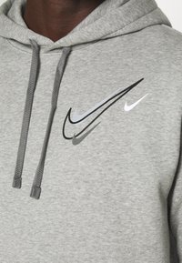 Grijze hoodie van textuurstof, met meerdere Nike swoosh-logo's in zwart, grijs en wit. Trekkoorden in bijpassend grijs.