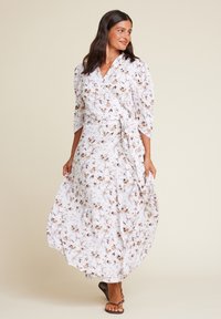 Omslagkjole i lett stoff med blomstermønster i brunt og beige på hvit bakgrunn. Lange ermer og knytebånd i midjen.