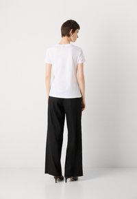 White short-sleeve t-shirt paired with high-waisted, black wide-leg pants. Features smooth fabric and understated design. High-heeled shoes.