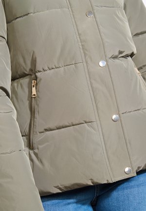Veste matelassée vert olive avec un design en piqué, boutons-pression métalliques et une poche zippée sur le côté. Texture lisse et matériau robuste.