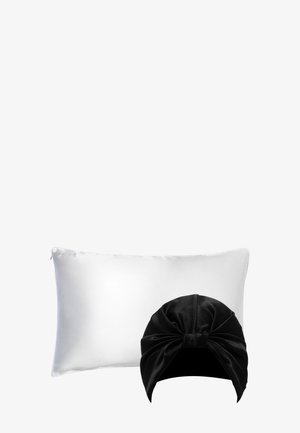 Coussin en satin blanc avec fermeture éclair arborant le logo « SILKE » et un bandeau en satin noir avec un design noué sur le dessus.