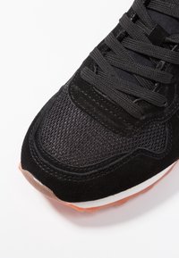 Svart sneaker med en texturerad mesh- och mockaöverdel, runda snörningar och en gummisula med en orange accent. Ren design utan synliga logotyper.