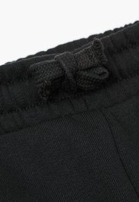 Schwarze Stoffshorts mit weicher Textur, ausgestattet mit einem gestrickten Bund und einem gewobenen Schleifchen. Eine Nahaufnahme hebt das Material und die Verarbeitung hervor.