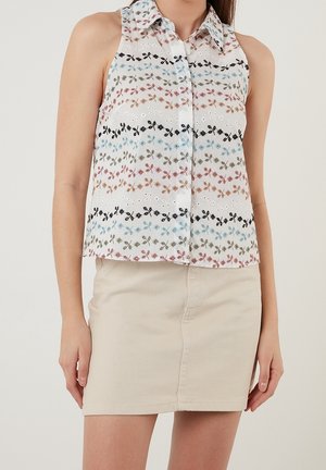 Haut sans manches et col en blanc avec une broderie florale multicolore en rayures horizontales ; associé à une jupe en denim beige clair.