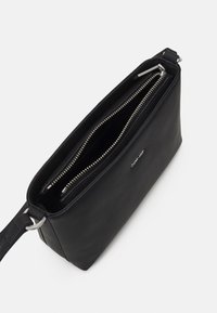 Černá kožená taška se zipovým uzávěrem, se stříbrným kováním, dvěma odděleními a plochým obdélníkovým tvarem. Hladký povrch.