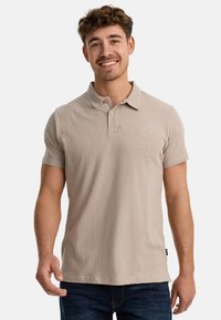 Helles beiges Poloshirt aus weicher Baumwolle, mit klassischem Kragen, kurzen Ärmeln und einem kleinen gestickten Logo auf der Brust.