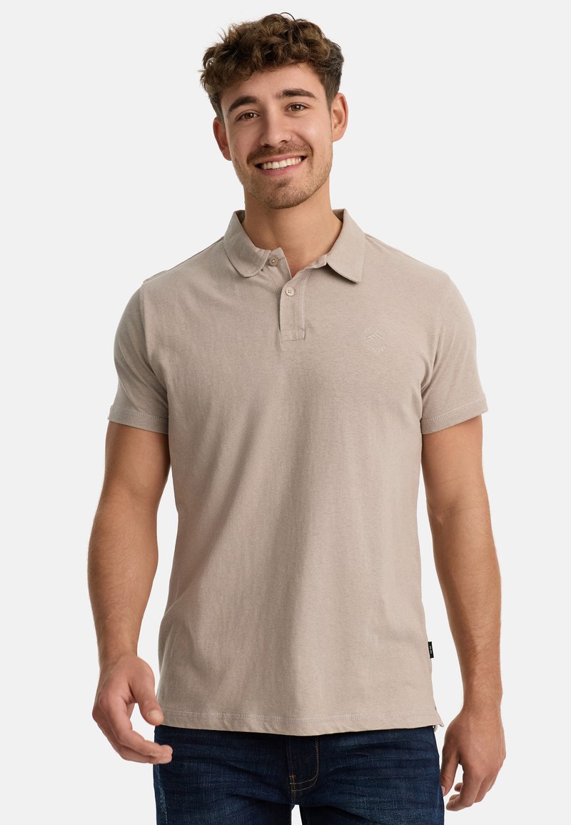 Polo de color beige claro fabricado en suave algodón, con un cuello clásico, mangas cortas y un pequeño logo bordado en el pecho.