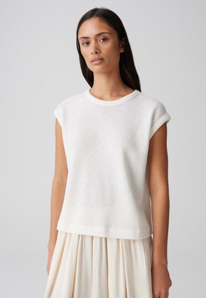 Top corto a maniche corte in maglia bianca con scollatura tonda, caratterizzato da un tessuto testurizzato e una vestibilità comoda, abbinato a una gonna fluida color crema.