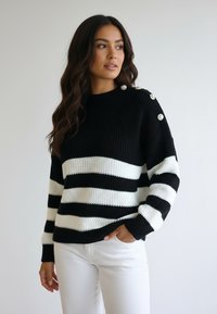 Czarnobiały sweter w paski, dziergany, z okrągłym dekoltem, ściągaczami na rękawach i dekoracyjnymi guzikami na ramieniu. Teksturowana tkanina.