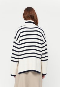 Maglione a righe in crema e blu navy, con colletto alto, vestibilità ampia, polsini a coste e orlo leggermente curvo.