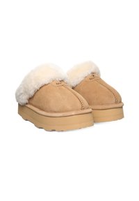 Jasnobrązowe skórzane klompy z puszystym, kremowym wykończeniem, charakteryzujące się przeszytym szwem, płaską podeszwą oraz metką z logo z boku.