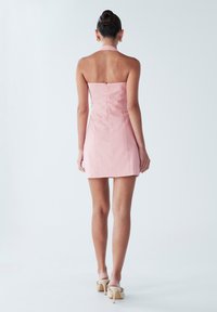 Roze halter mini-jurk met een getailleerd lijfje en ritssluiting aan de achterkant. Gladde stof met strakke lijnen en minimale details.