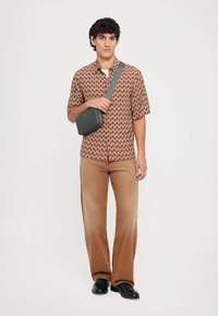 Lysbrun mønstret kortærmet skjorte, tan bredbenede bukser, sorte sko og en grå crossbody taske. Enkel, afslappet design.