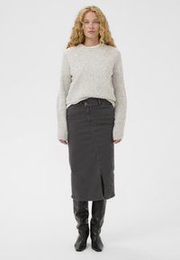 Šedý pletený sveter s dlhými rukávmi skombinovaný s tmavomodrou džínsovou midi sukňou s predným rozparkom. Modelka má na sebe čierne vysoké čižmy.