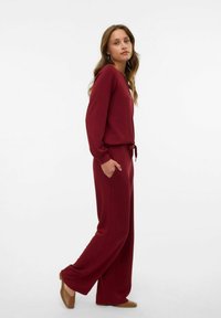 Bordeaux loungewear set met een lange mouw top met een ronde hals en elastische taillebroek met zakken. Zachte stof, ontspannen pasvorm.