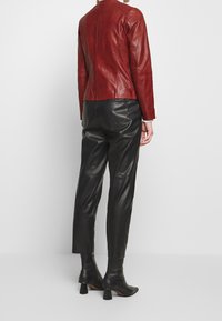 Röd läderjacka med figursydd passform, detaljering i bakseam, kombinerad med högmidjade svarta läderbyxor och ankelstövlar.