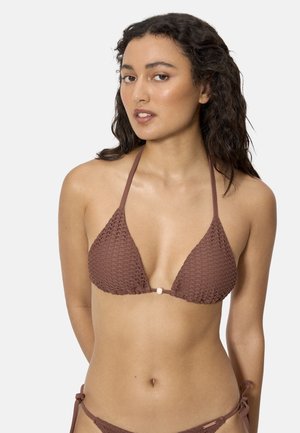 Mujer joven con cabello largo y oscuro que lleva un bikini de halter marrón texturizado con braguitas a juego con lazo lateral, sobre un fondo liso.