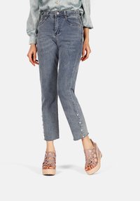 Jeans azzurri a vita alta con orlo sfilacciato e bottoni in perla, abbinati a sandali a piattaforma intrecciati color lavanda.