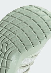 Gros plan d'une semelle de chaussure vert clair avec un motif texturé en grille pour l'adhérence et une partie supérieure en mesh blanc visible.