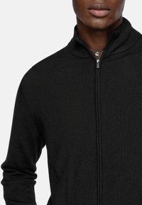 Black zip-up sweater featuring a high collar, ribbed texture, and fitted sleeves, with a smooth, lightweight fabric and silver hardware.