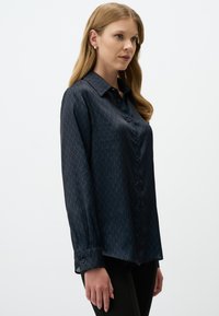 Dark blue button-up shirt with a diamond pattern, long sleeves, and a collar. Made of a smooth, shiny fabric. Features dark buttons.