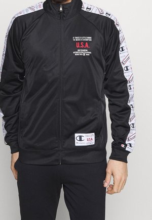 Giacca a track nera con zip, dettagli in logo bianco e rosso, con accenti decorativi sulle maniche e un'etichetta in tessuto all'orlo.