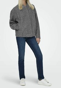 Chaqueta gris, texturizada y de gran tamaño con un cuello, cierre frontal a presión, combinada con vaqueros azules y zapatillas blancas. Ajuste casual y relajado.