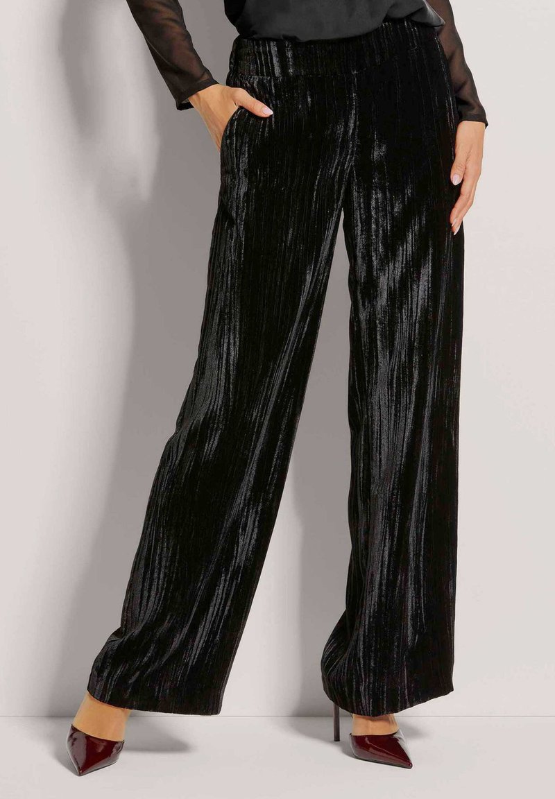 Zwarte fluwelen wijde broek met verticale ribbelstructuur en dubbele zijzakken. Heeft een zachte tailleband en kan gecombineerd worden met puntige hakken.