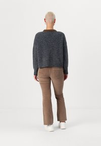 Pull gris court avec col marron, associé à un pantalon en velours côtelé évasé marron clair. Modèle portant des baskets blanches, vu de dos.