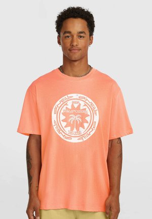 Kortærmet, oversized t-shirt i lys koral, med et hvidt grafisk design af palmer og et cirkulært logo foran.