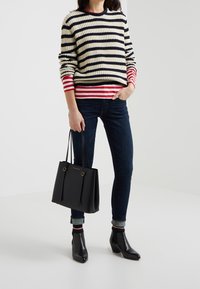 Pull en maille rayé crème, marine et rouge, associé à un jean foncé et des bottines noires. Tient un sac fourre-tout noir avec des accents dorés.