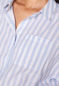 Light blue and white striped short-sleeve shirt, featuring a button-down collar and a patch pocket on the left side. Soft fabric texture.