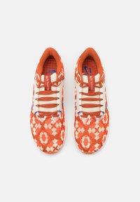 Buty do biegania z czerwono-białym kwiatowym wzorem, cholewką z teksturowanego dzianego materiału oraz kontrastującymi niebieskimi akcentami na logo i sznurowadłach.