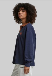 Marine langermet polo skjorte med brun krage og tre-knappers placket; har et brodert logo på brystet; avslappet passform.