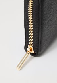Zwart leren rits etui met een gestructureerde afwerking. Voorzien van een gouden rits en accent, met een strak rechthoekig ontwerp.