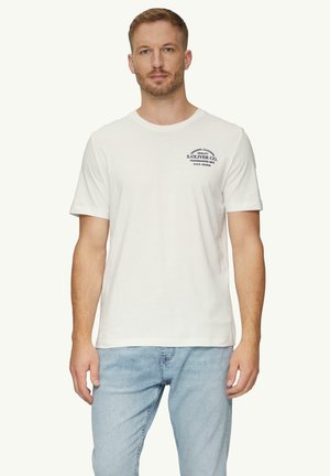 T-shirt en coton blanc à manches courtes, avec un logo bleu marine sur la poitrine gauche. Porté avec un jean en denim bleu clair.
