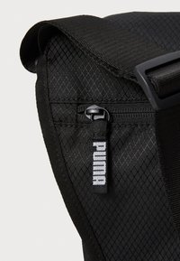 Sac à dos noir avec un motif en diamant texturé, comportant une poche zippée et une étiquette avec le logo PUMA. Les bretelles sont ajustables et robustes.