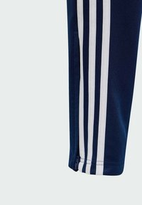 Marineblauwe sportbroek met drie witte strepen aan de zijkant, rits aan de onderkant en textiel dat comfort en duurzaamheid biedt.