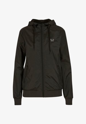 Chaqueta negra con capucha y cierre frontal, puños y dobladillo elásticos. Presenta un pequeño logotipo de mariposa en el lado izquierdo del pecho y una textura suave y brillante.