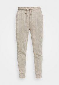 Pantalons de jogging à carreaux beiges avec une taille élastique, un cordon de serrage et un tissu texturé présentant des carrés alternant textures et surfaces lisses.