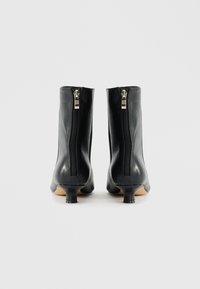 Bottes de cheville en cuir noir au design épuré, dotées d'une fermeture éclair à l'arrière et de petits talons effilés. Texture lisse et accents minimaux.