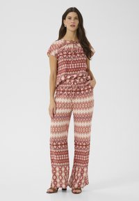 Ensemble à motifs rouge et crème comprenant un top court avec des accents froncés et un pantalon large à motifs géométriques. Texture du tissu lisse.