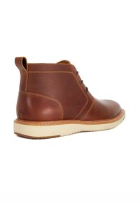 Brown leather ankle boot with a smooth finish, white rubber sole, minimal lacing, and a pull tab for easy wear. Features contrast stitching.