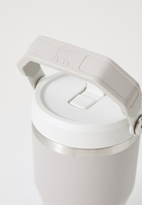 Insulated travel mug with a matte light gray finish, stainless steel rim, white lid, and a textured gray handle featuring a logo.