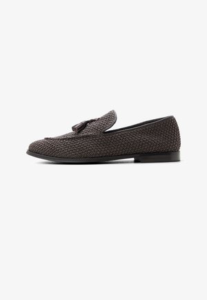 Donkerbruine gevlochten loafer met platte zool en kwastdetail bovenop, getoond vanaf de binnenkant tegen een witte achtergrond.