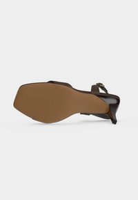 Sandale à talon en cuir marron montrant une semelle lisse et une bride de cheville réglable avec boucle métallique sur fond blanc.