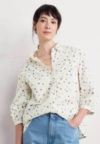 Knapp-up skjorta i krämfärg med lila och gröna prickar, med krage, långa ärmar och avslappnad passform, bärs med ljusblåjeans.